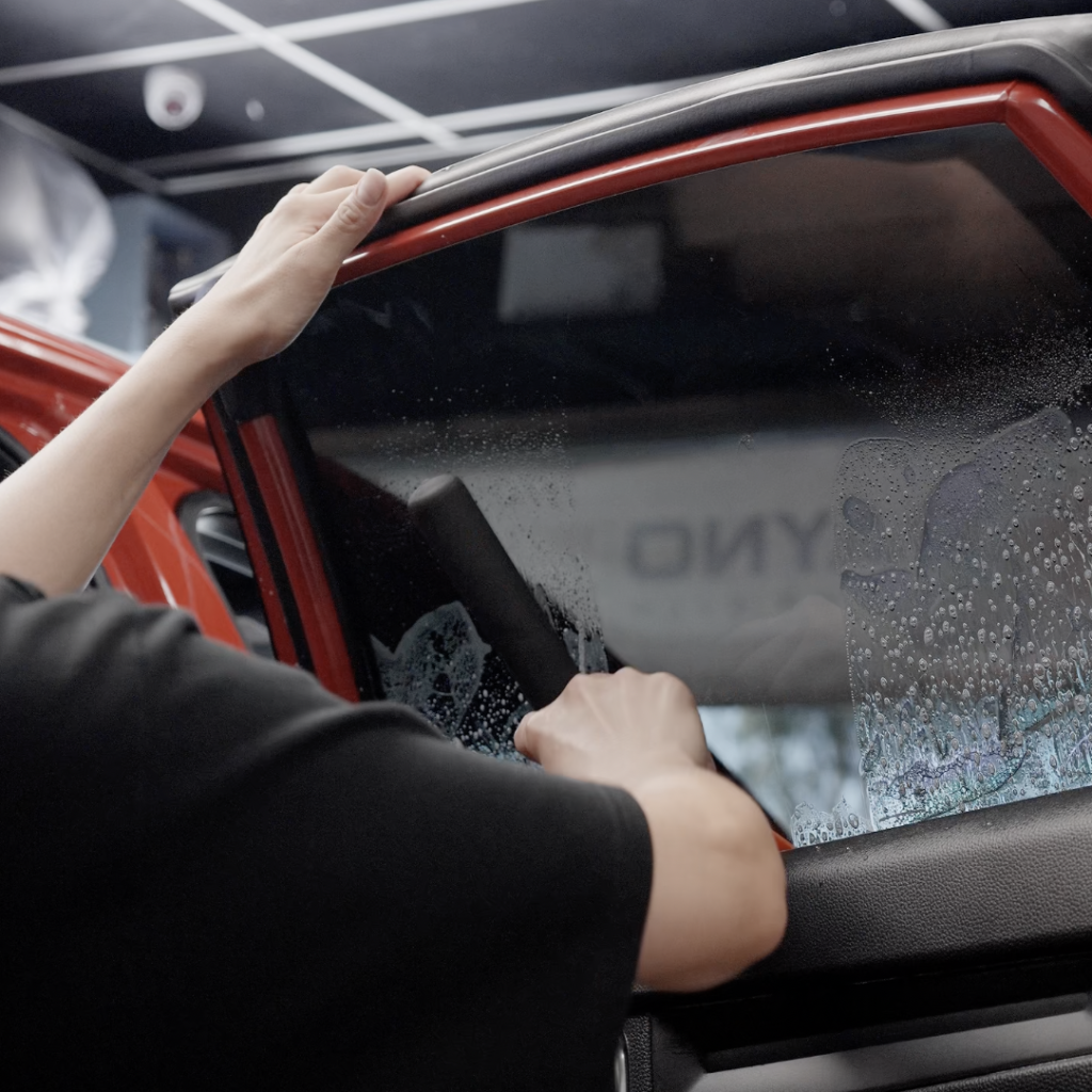 Technician installing tint on car door window at Downey Tinting